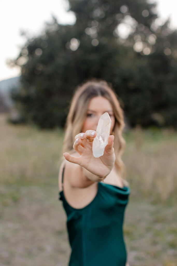 Alessia stands in a pasture holding a Lemurian Seed crystal while wearing a green dress. The crystal is in focus, creating depth of field with Alessia out of focus in the background.